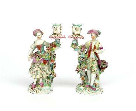 A pair of Derby candlestick figures of vintners  c.1765, he standing beside a basket of grapes and other fruit, his companion