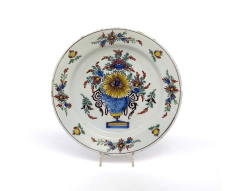 A delftware charger  c.1740, painted in polychrome enamels with a large vase of flowers to the well, the rim with flower spra