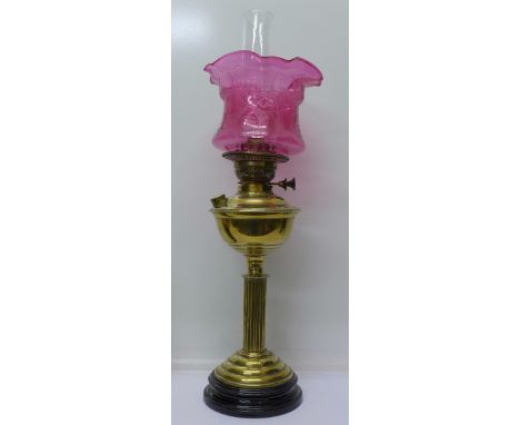 A brass oil lamp with cranberry glass shade, 65cm