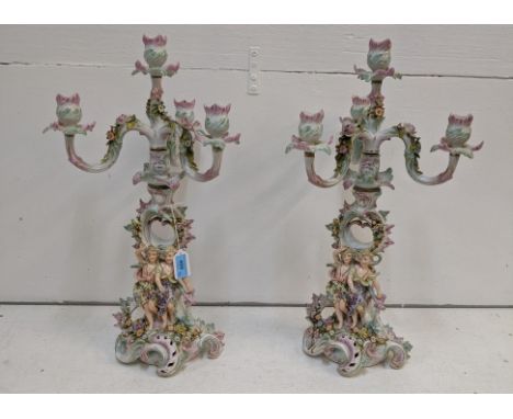 A pair of Sitzendorf four branch candelabras ornately decorated with flowering plants and gilt swirls with two cherubs on eac