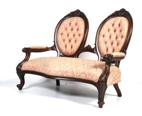 A Victorian carved mahogany two-seat parlor sofa. Of serpentine form, upholstered in pale peach/pink damask, with twin oval s