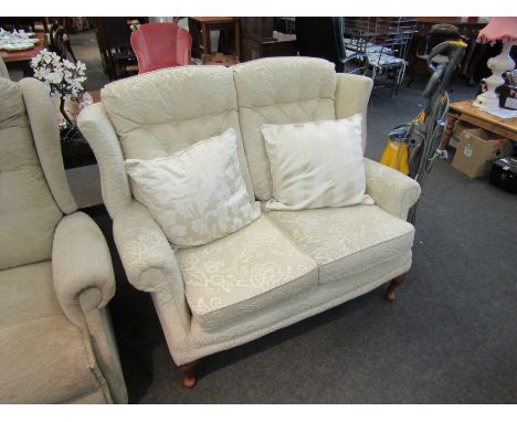 A modern wingback two seater sofa with loose cushions in cream velour upholstery