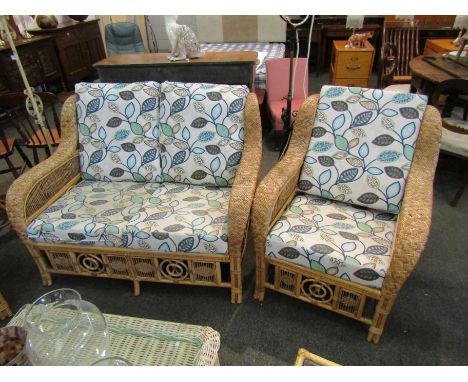 A cane conservatory suite with leaf pattern upholstery, two seater sofa, pair of chairs and two side tables