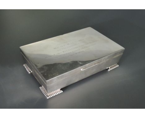 A silver cigarette box of plain casket form having bracket feet and presentation inscription regarding The Hong Kong Telephon