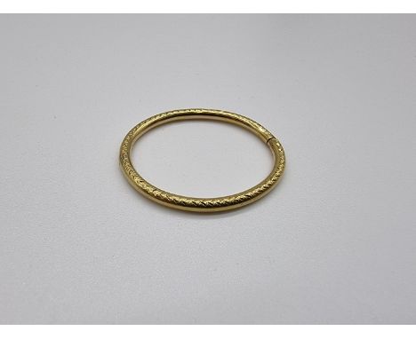 A yellow metal child's hinged bangle, stamped K18, having chased decoration, 4g. 