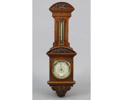 A late 19th century aneroid wall barometer with a 7” diameter white enamel dial, &amp; in a carved walnut case, 40¾” high. 