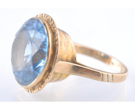 A 9ct gold and spinel Etruscan style ring. The ring being set with a large pale blue synthetic spinel within a tall ribbed be