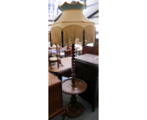 A carved wooden standard lamp, with barley twist stem and undertier with yellow fringed shade 