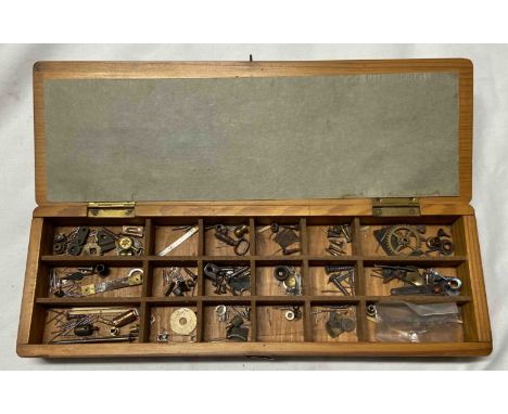 A vintage wooden box with interior compartments containing clock and watch making components