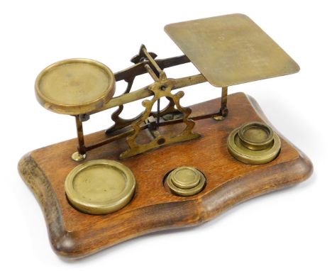 A set of early 20thC brass postal scales, on a wooden base with inscription postage rates for letters with an assortment of f
