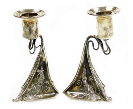 A pair of Arts and Crafts style silver candlesticks, with tapered stem, on shaped body with artistic applied scroll detailing