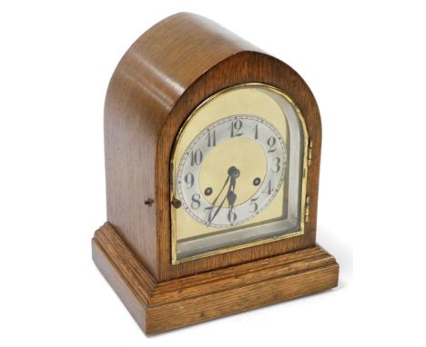 An early 20thC oak cased mantel clock, with arched central brass dial, on a staggered base, 29cm high, 23cm wide, 17cm deep.