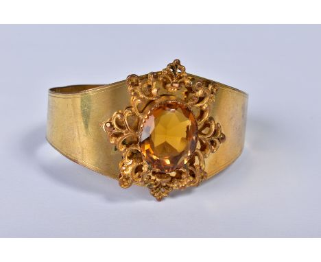 A VICTORIAN GILT METAL BANGLE, the foliate scroll mount set with a central facet cut citrine, tapering bangle with hook clasp