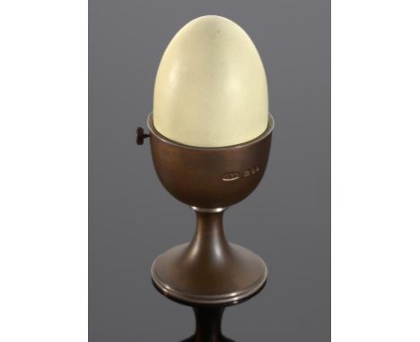 AN ANTHONY ELSON SILVER GILT AND ENAMEL 'TROMPE L'OEIL' EGG IN AN EGG CUP containing parcel gilt and clockwork merry-go-round