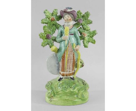 Standing before bocage, holding a bow and arrow, quiver at her hip and straw target at her feet, wearing brightly coloured co
