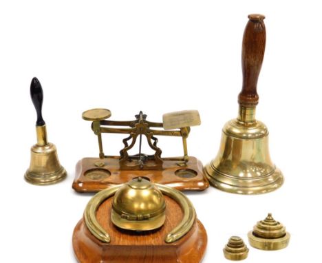 A group of brass ware, to include a set of postal scales on an oak base with various weights, 20cm wide, two hand bells, and 