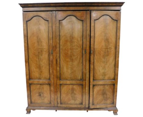 An early 20thC Georgian style mahogany triple wardrobe, the outswept pediment over three doors, enclosing hanging rails, rais