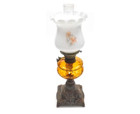 An early 20thC oil lamp, with an opaque shade decorated with flowers, an amber glass central reservoir on a cast iron base, w