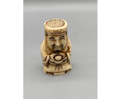 A Japanese hand carved bone netsuke of an elderly gentleman holding a token. Signed. [5.2cm in height] 