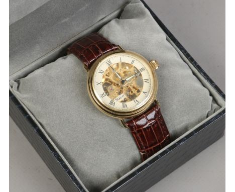A Stauer manual wind skeleton wristwatch Roman numeral baton markers polished brass case iluminos fingers.