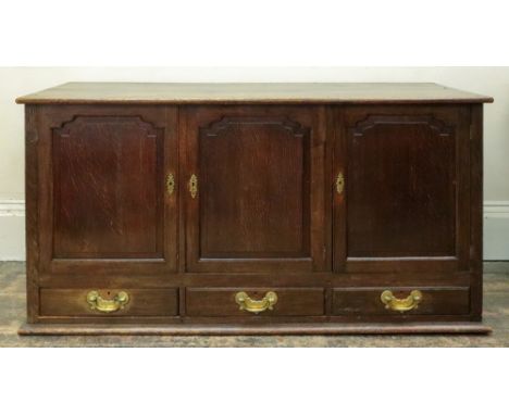 A reproduction George III style oak dwarf cupboard, enclosed by three shaped raised and fielded panel doors with three drawer