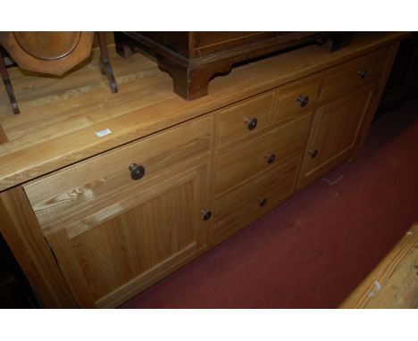 A contemporary light oak sideboard having an arrangement of six drawers and twin recessed panel cupboard doors, 180cm