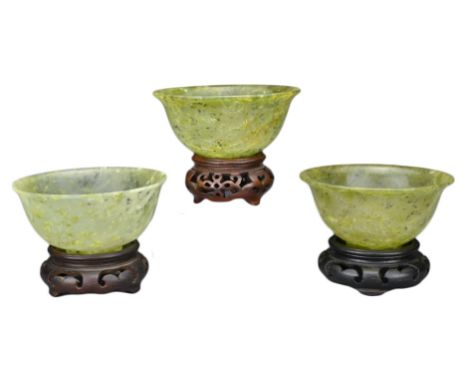 THREE CHINESE 'SPINACH JADE' BOWLS ON STANDS, 20TH CENTURY. Each bowl with rounded body on a shallow foot with everted rim on