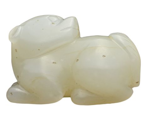 A CHINESE PALE CELADON JADE CARVING OF LION DOG. The recumbent animal with its legs tucked under its body with its head turne