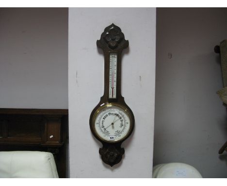 An Early XX Century Oak Aneroid Barometer, shaped top, with a carved flower, temperature gauge, porcelain barometer dial.