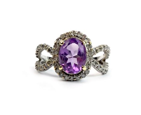 AMETHYST AND DIAMOND RING, set with a central oval faceted amethyst 8.7mm long, within a diamond halo, on open elliptical dia
