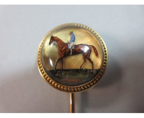 A reverse carved and painted crystal stick pin depicting a race horse with jockey up, the chestnut horse walking on a grassy 