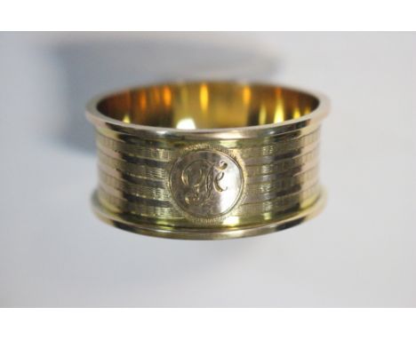 A yellow metal napkin ring, stamped 9ct, circular with engine turned decoration, engraved 'F' in cartouche, 45mm diameter, 23