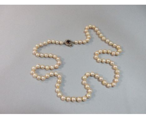 An opera length pearl necklace with garnet and seed pearl clasp, the uniform 8mm cultured pearls of creamy-peachy hue, indivi