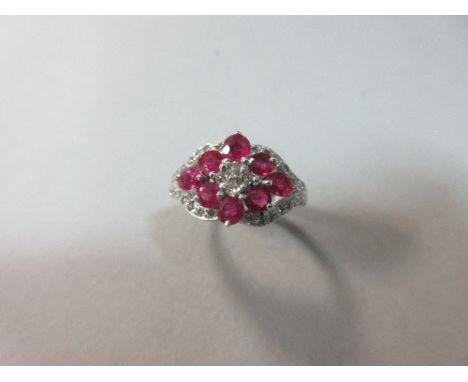 A ruby and diamond ring, the eight round and oval cut rubies arranged in a horozontal diaper pattern around a cluster of four