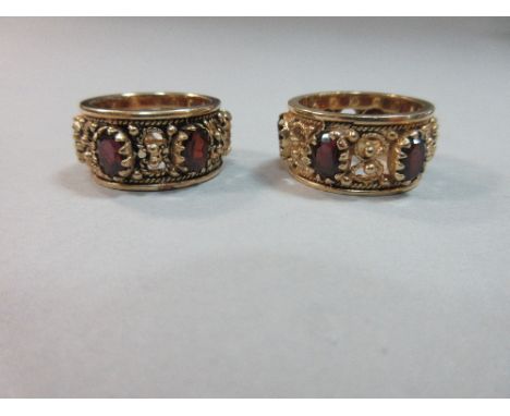 A pair of ornate garnet band rings, each a uniform 12mm wide and set with six oval cut garnets separated by pierced figures o