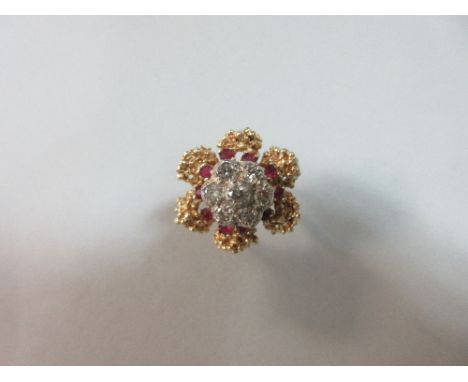 A diamond and ruby flower ring, the central close set cluster of seven round brilliant cut diamonds in a flowerhead formation