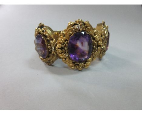 A 19th century amethyst and repoussé work broad hinged bangle, set to the front with three graduated large oval cut amethysts