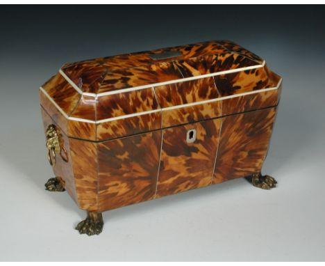 A Regency tortoiseshell tea caddy, the sarcophagus form with lion mask handles and raised on paw feet, the fitted interior wi