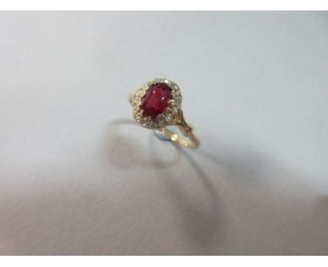 A ruby and diamond cluster ring, the oval cut ruby in a border of fifteen rose cut diamonds to X-figure shoulders and a plain