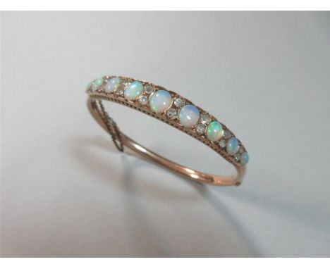 An opal and diamond hinged bangle, the front section set with graduated oval cabochon opals separated by pairs of old round c