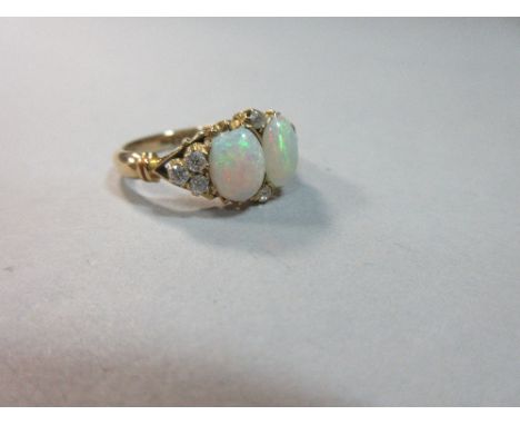 An Edwardian 18ct opal and diamond ring, set with two oval cabochon opals with trios of old round cut diamonds either side an