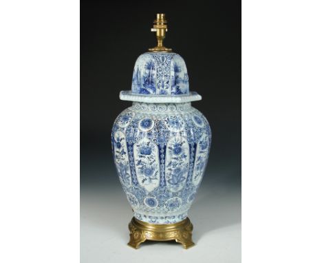 A gilt metal mounted Delft blue and white covered vase as a lamp, the ribbed ovoid body painted with panels of flowers and th