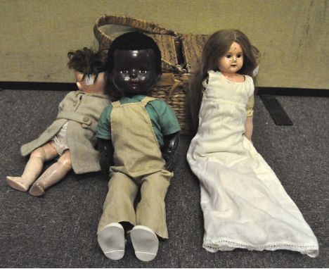 A vintage wicker picnic basket containing various dolls, including a Heubach-Koppelsdorf doll, no. 320, a Black Pedigree doll