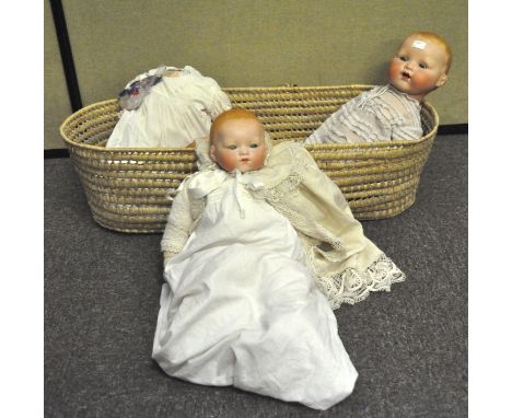 A vintage wicker basket containing three German (Armand Marseille) bisque dolls, including one numbered 351/9K, mostly clothe