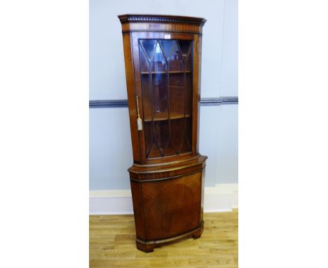 A reproduction mahogany corner cabinet, having astragal glazed panel door to top, enclosing shelved interior above panel door