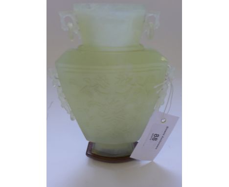 A Chinese carved jade twin handled vase, with stylised foliage in relief, on a shaped hardwood stand.  18cm high