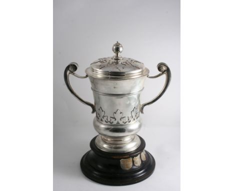 AN EDWARDIAN TROPHY CUP & COVER with two harp-shaped handles, cut-card decoration & a bud finial, engraved on one side with a