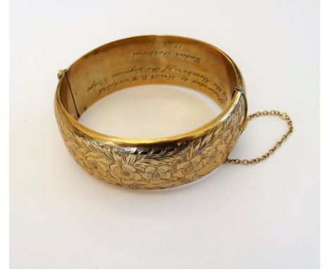 A 9ct gold hollow bangle of oval form, engraved to one side with repeat flowerheads and foliage, the inner band presentation 