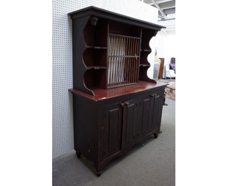 A distressed red and black painted pine dresser, the enclosed shelf back with fitted plate rack over four raised panel doors,