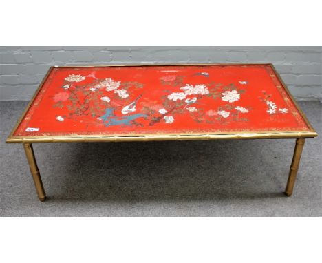 A Chinese red lacquer panel topped low table, with painted floral decoration on simulated bamboo brass frame base, 120cm wide